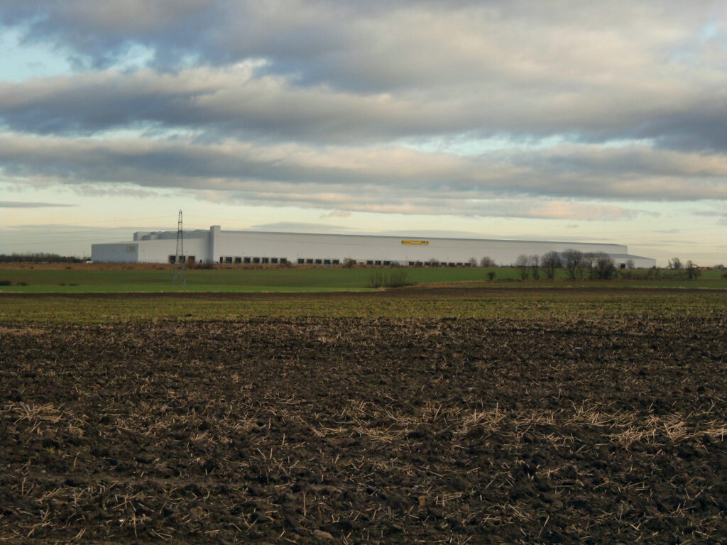 A vast distribution warehouse looming over ploughed farmland